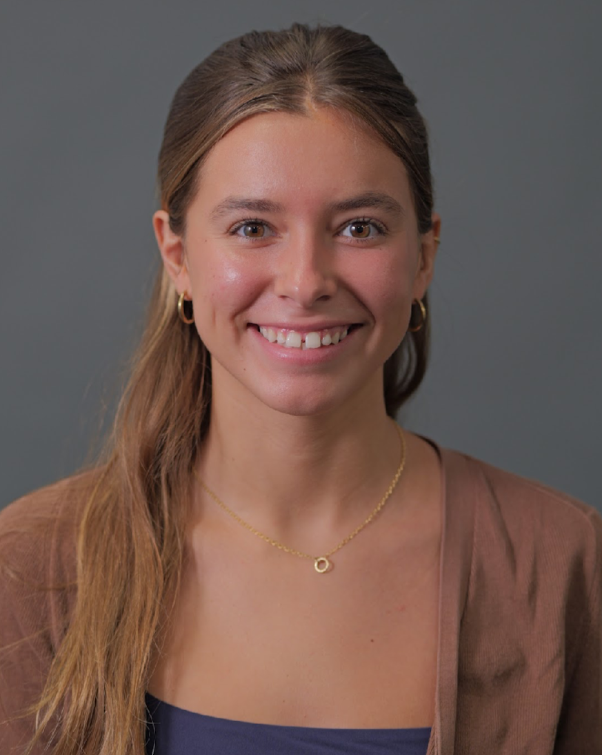 Kylie has long, light brown hair and is smiling for a photo, wearing a brown cardigan over a black shirt