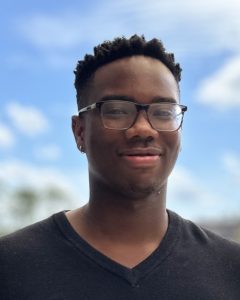 Moustapha smiles for a photo, he is wearing glasses and a black shirt