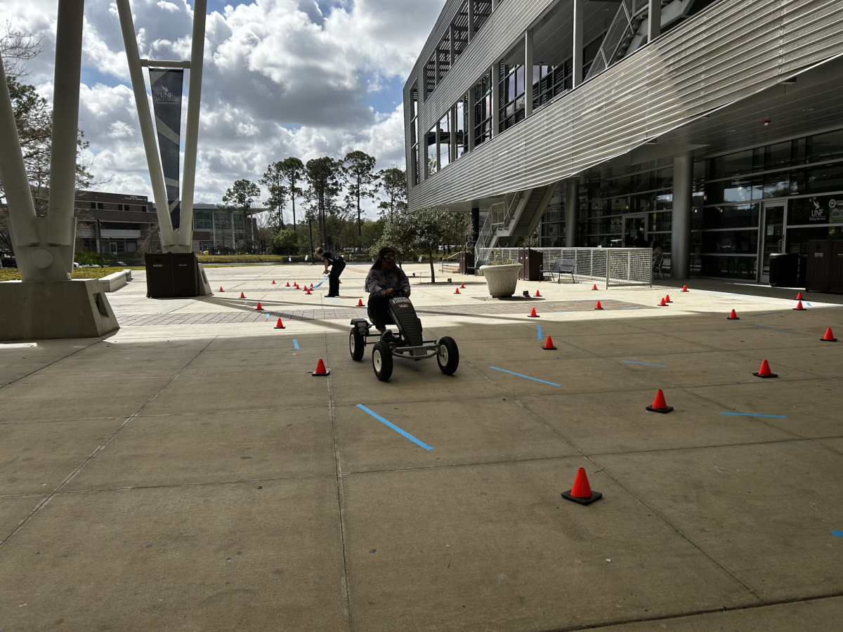 Riley Skinner uses the pedal cart on the drunk driving simulator course while Karen Livingston prepares the course for the next driver.