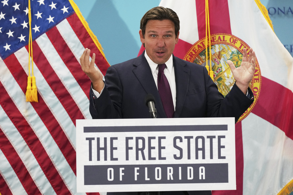 Florida Gov. Ron DeSantis speaks during an event at a podium that reads "The Free State of Florida" with his arms raised in the air.