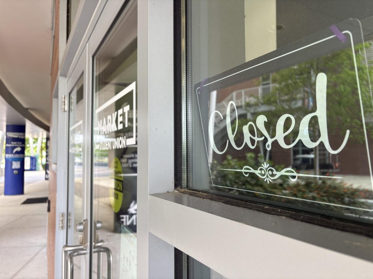 A black and white "Closed" sign sitting in the window of one of the food convenience stores at UNF.