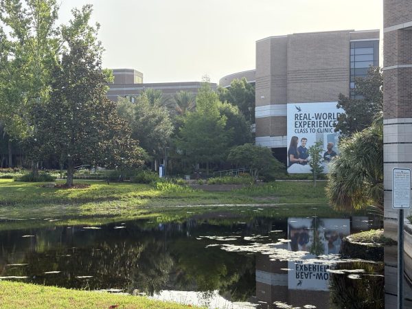 A lake in front of a UNF building surrounded by green grass and trees.