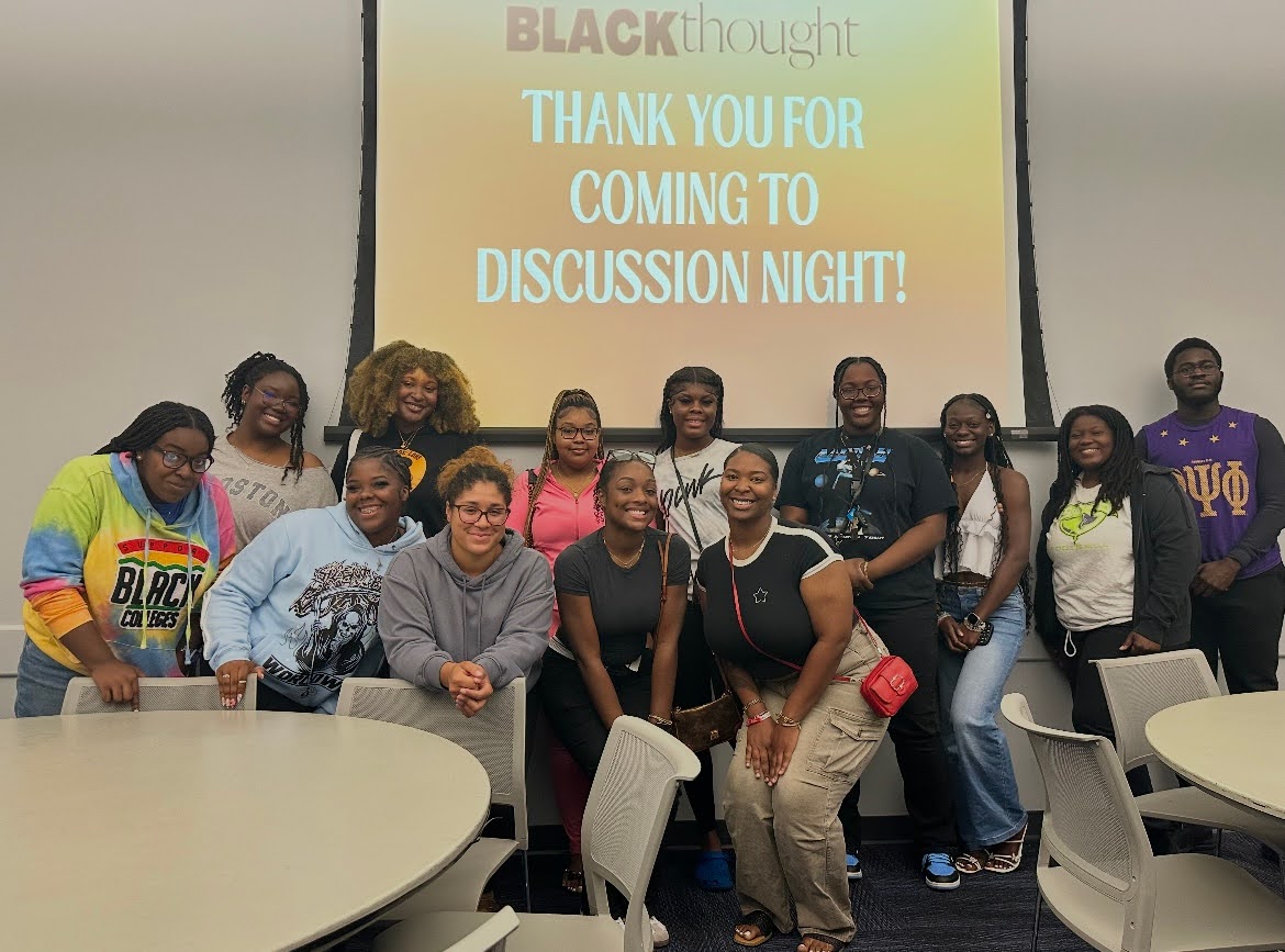 Black Thought Club members smile together in front of a screen at a discussion meeting.