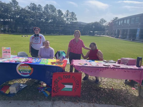 Four Pride Club members gather around a table smiling with colorful tablecloths and outfits