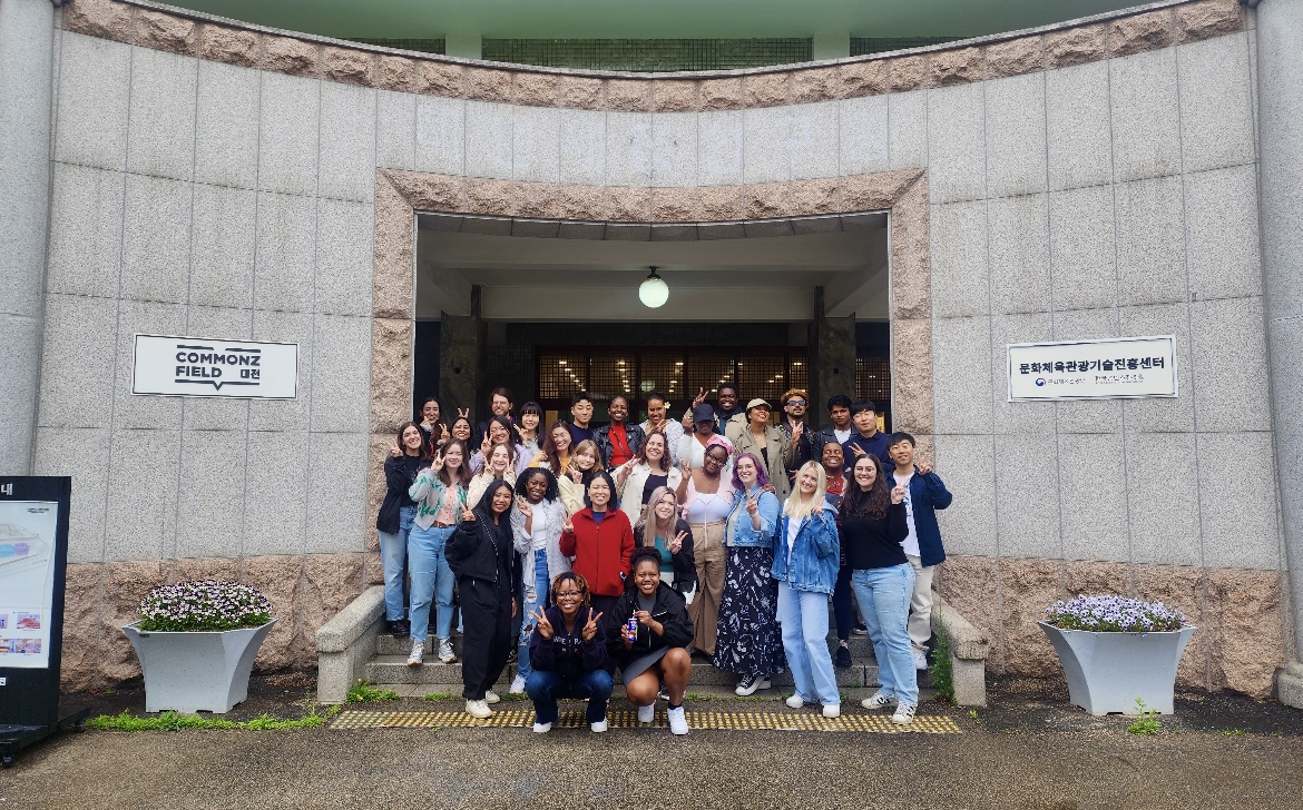 Students studying abroad in Daejeo, South Korea smile for a photo together underneath an arch on stair steps.