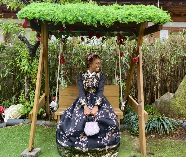 Anecia Francis sitting on a swing in South Korea in a long, black and white patterned dress.