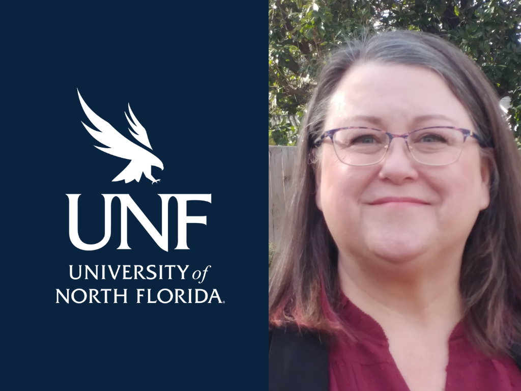 Dr. Kimberly Mayer is smiling with brown hair, glasses, wearing a black sweater and red blouse.