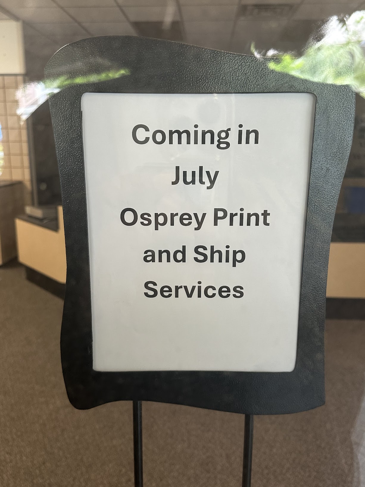 A white sign reads, "Coming in July Osprey Print and Ship Services."