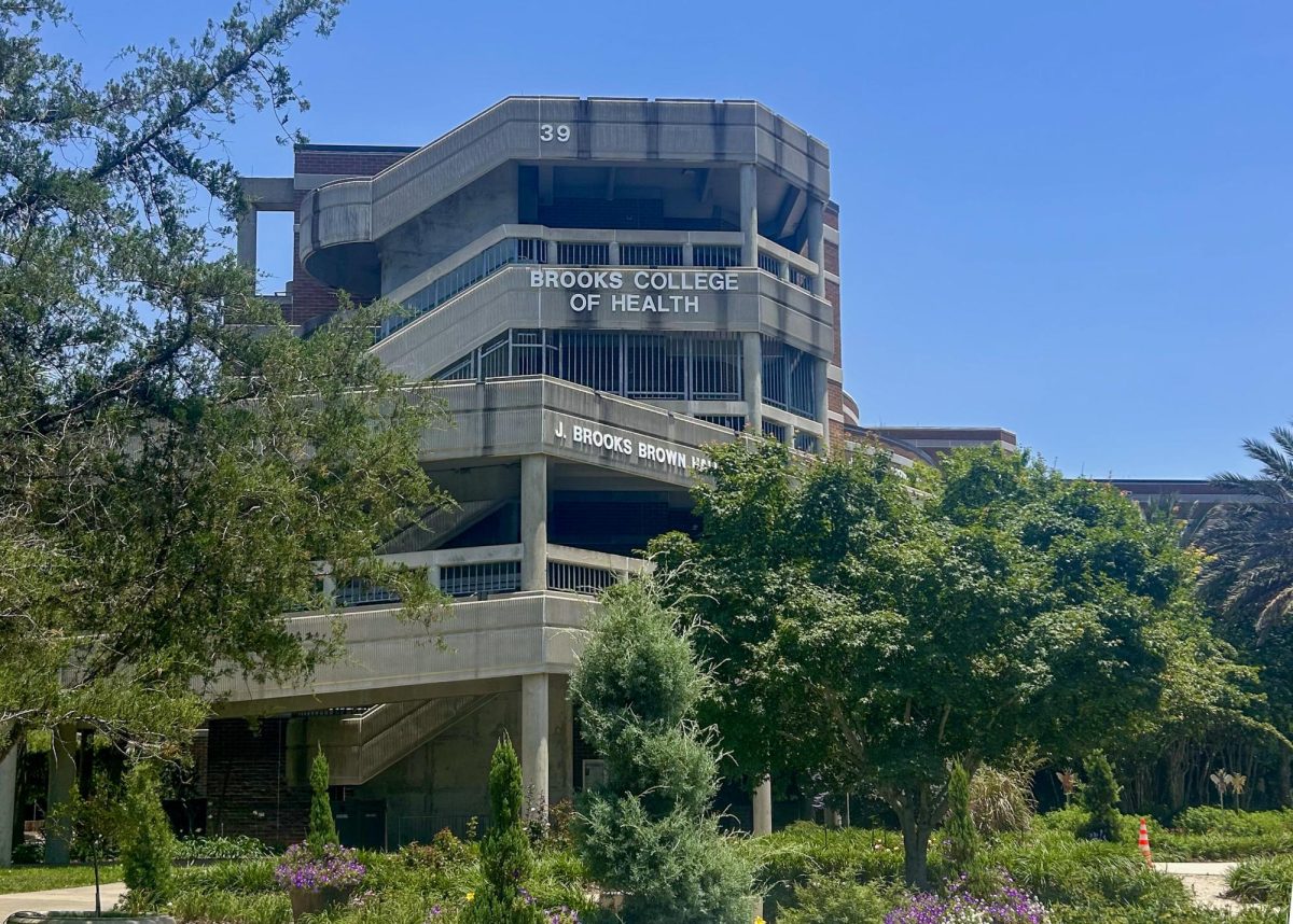 A multi-level brick and concrete building titled the "Brooks College of Health" sits behind multiple trees and plants.