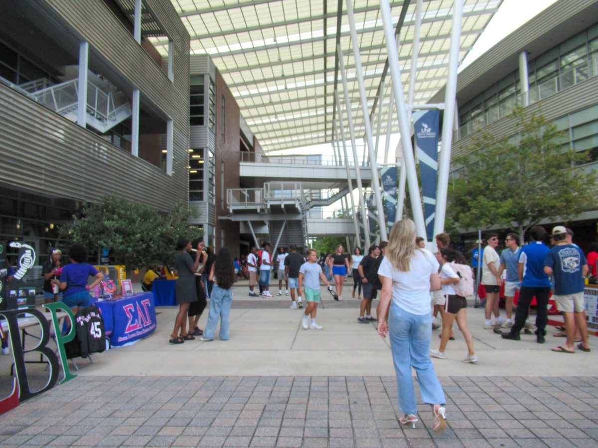 A group of people are standing under large brick and glass buildings.