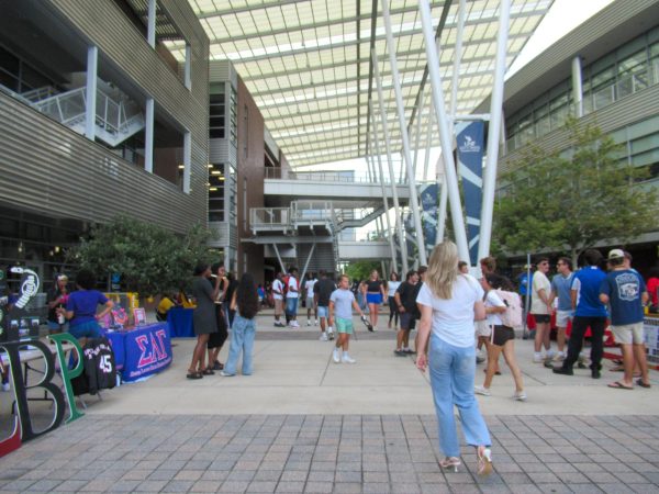 A group of people are standing under large brick and glass buildings.