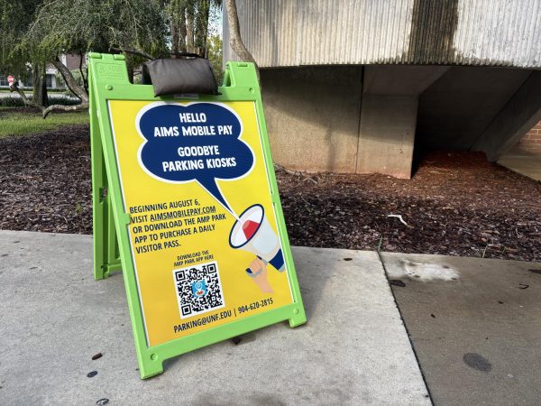 a bright green A-frame sign outside the UNF parking garage with information on how to use the new AIMS Mobile Pay App