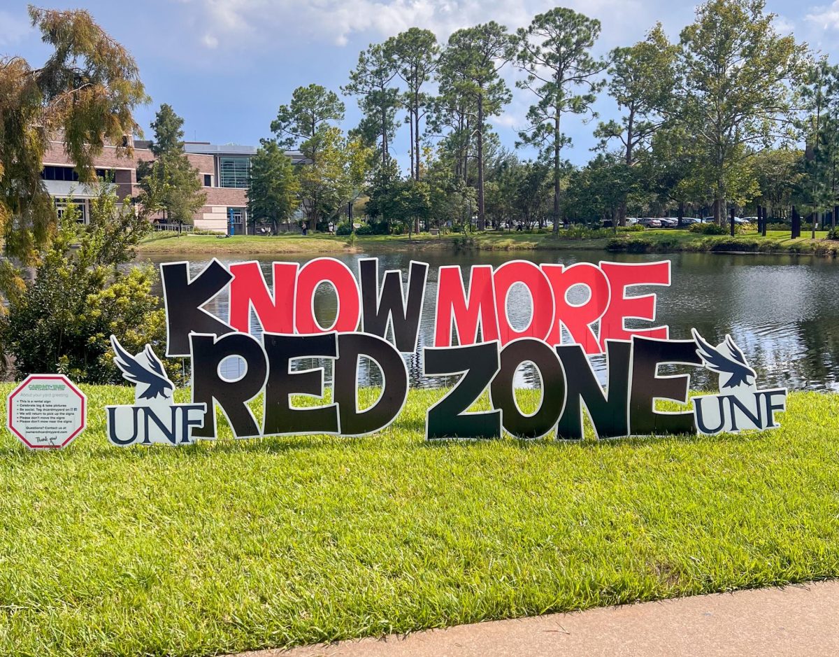 A black and red sign reading "Know More Red Zone" in front of a lake.