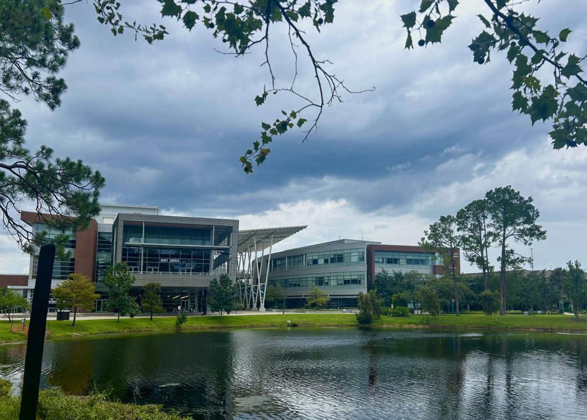 Two large metal and brick buildings sit next to each other on the other side of a lake.