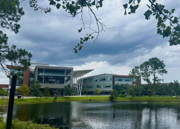 Two large metal and brick buildings sit next to each other on the other side of a lake.