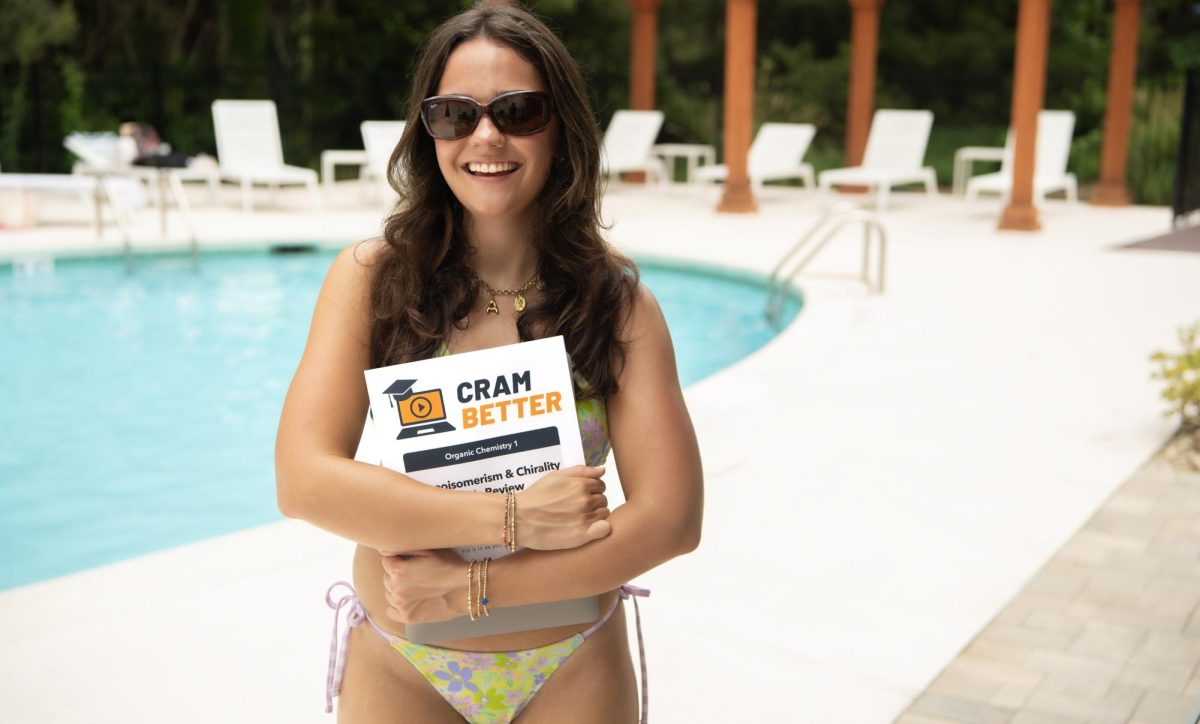 Female college student in sunglasses and swimsuit smiling by a pool holding a textbook that says "CramBetter" on the front cover.