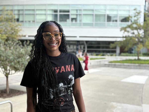 Daisia Carter is smiling, wearing brown glasses and a black graphic t-shirt.