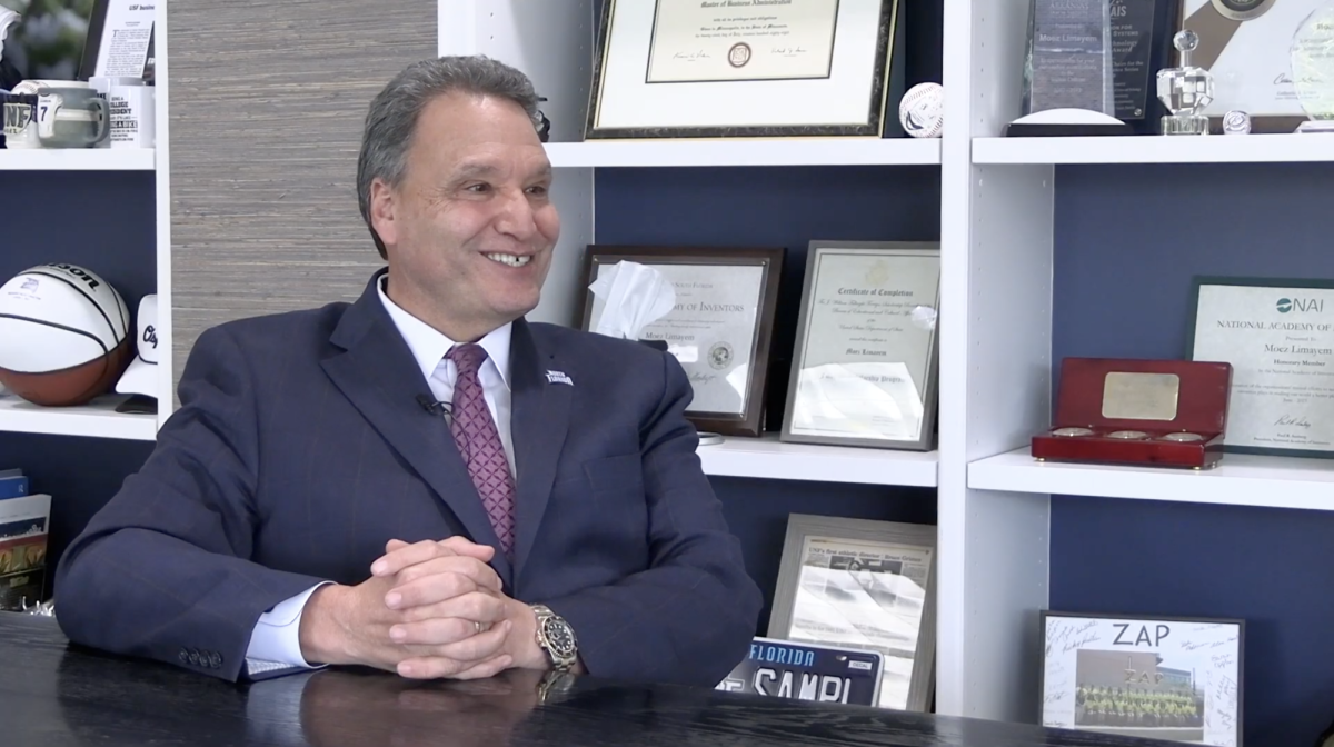 President Limayem speaks, smiling in a dark blue suit in his office.