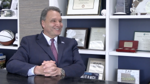 President Limayem speaks, smiling in a dark blue suit in his office.
