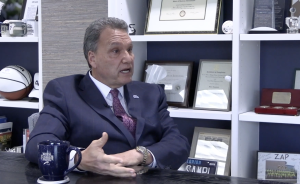 UNF President Limayem speaks, he's sitting in his office in front of a white book shelf wearing a dark blue suit.