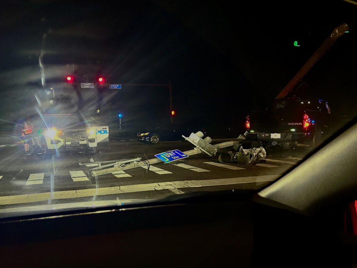 A police car is in an intersection at night. A black truck is on the right of the frame. A light post is lying on the ground.