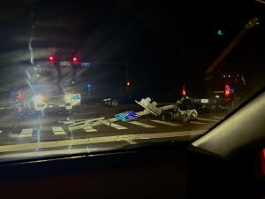 A police car is in an intersection at night. A black truck is on the right of the frame. A light post is lying on the ground.