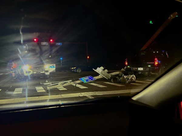 A police car is in an intersection at night. A black truck is on the right of the frame. A light post is lying on the ground.