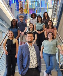 11 people dressed in business casual outfits stand on a staircase smiling at the camera.