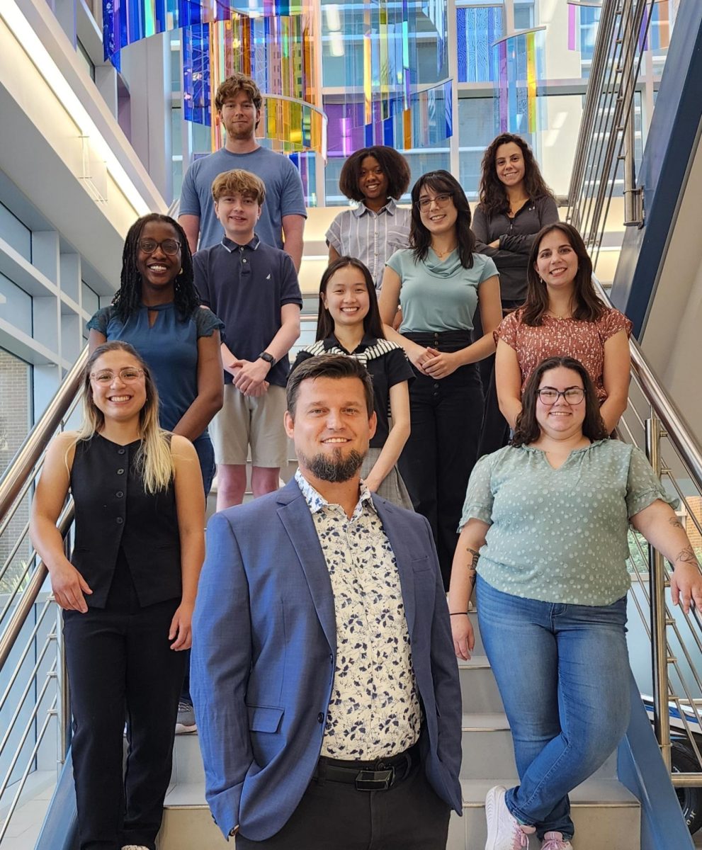 11 people dressed in business casual outfits stand on a staircase smiling at the camera.