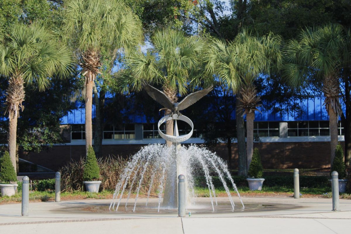 A fountain in front of palm trees with an osprey statue.