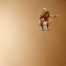 Man in red shirt and white shorts jumping with gold background