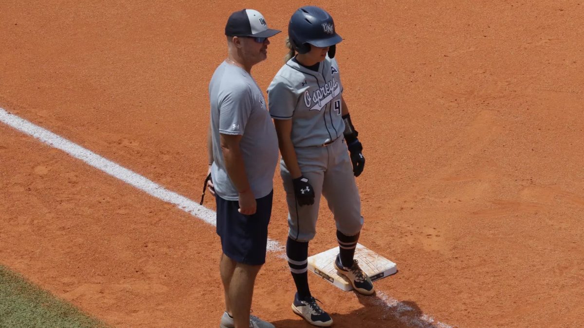 Softball player standing on plate with coach standing next to her.
