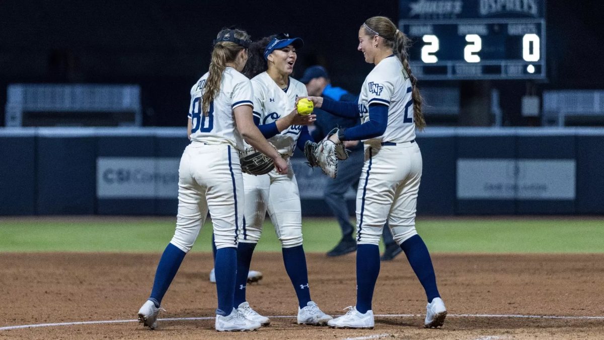 Three softball players circle around a yellow softball.