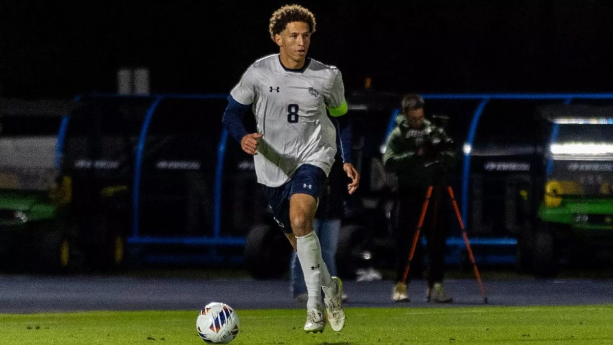 Black player in soccer uniform steps forward toward a white soccer ball. It's nighttime.