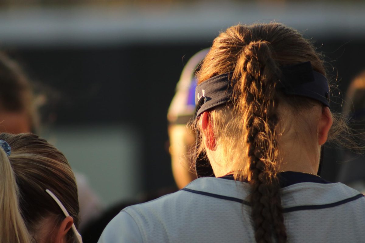 Back of softball players head. She has her hair up in a braided ponytail.
