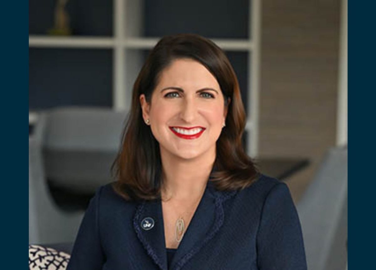 Woman with brown hair and red lipstick where navy blazer smiles at camera.