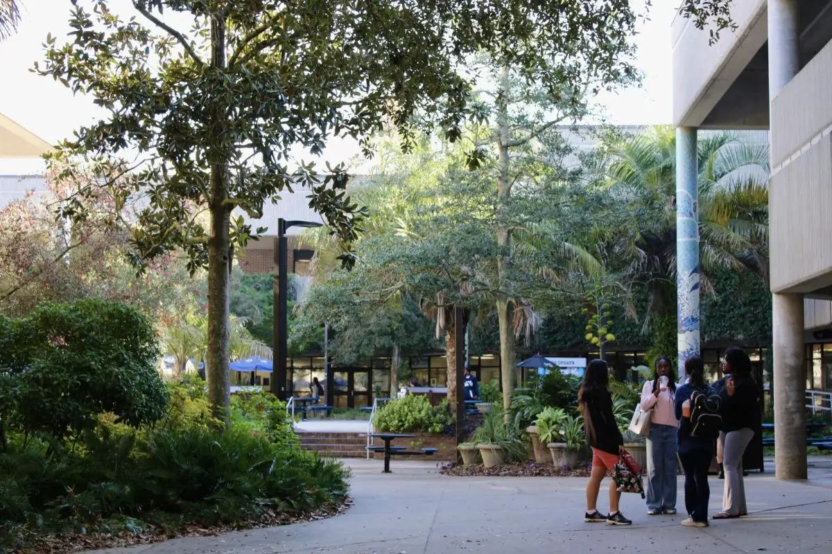 Some students stand in the UNF food court plaza where there's many trees and greenery.