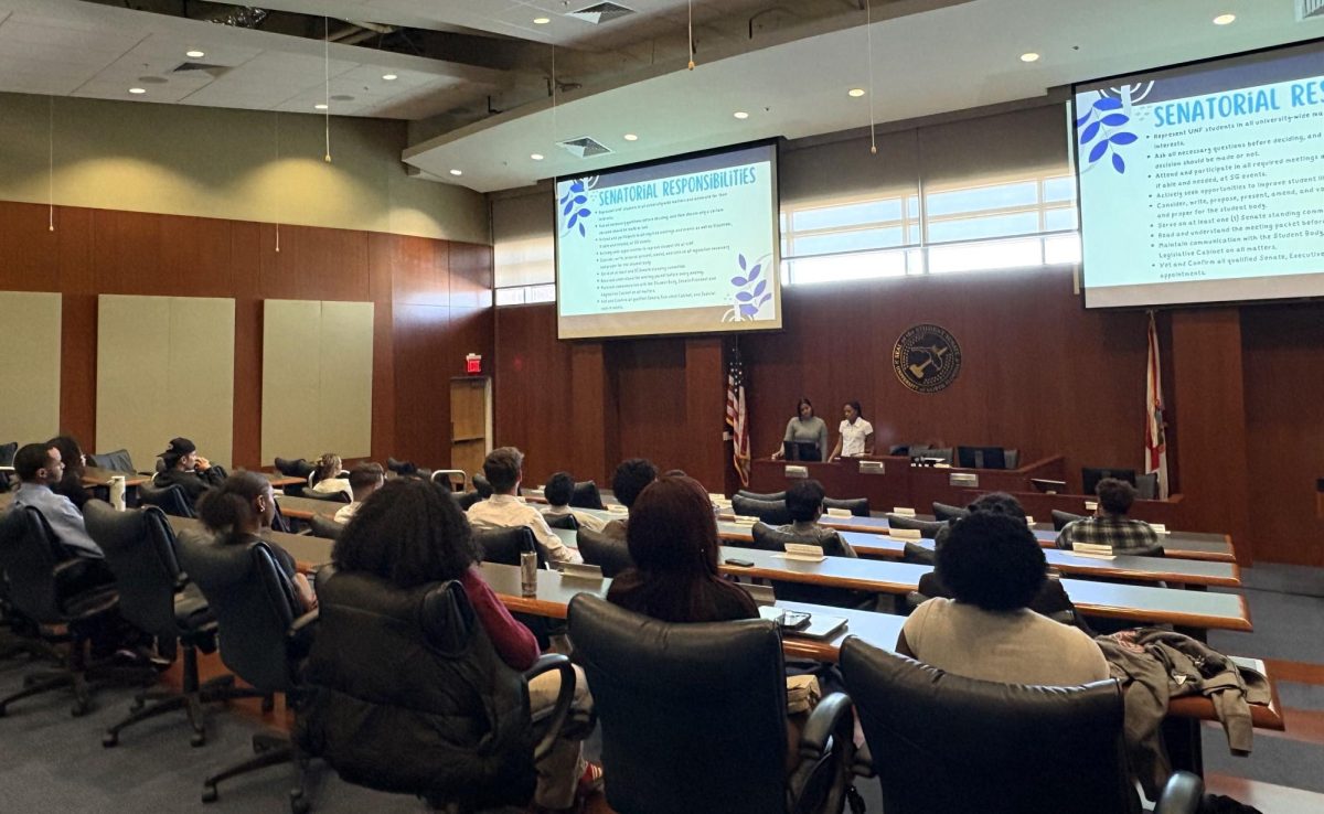 From the perspective of the back of the room, an open chamber room shows many students sitting in chairs as they view a powerpoint on a projector at the front of the room.