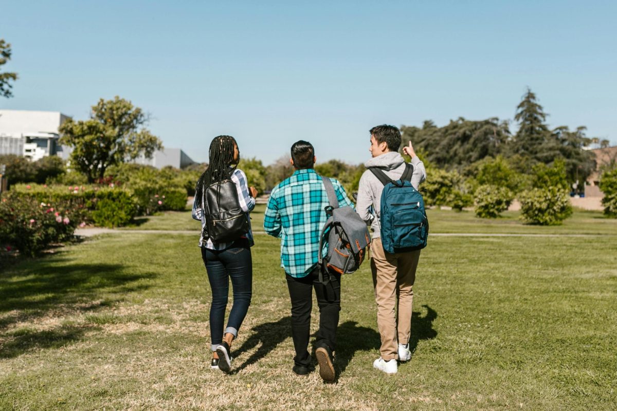 Three students wearing backpacks walking with their backs turned to the camera.
