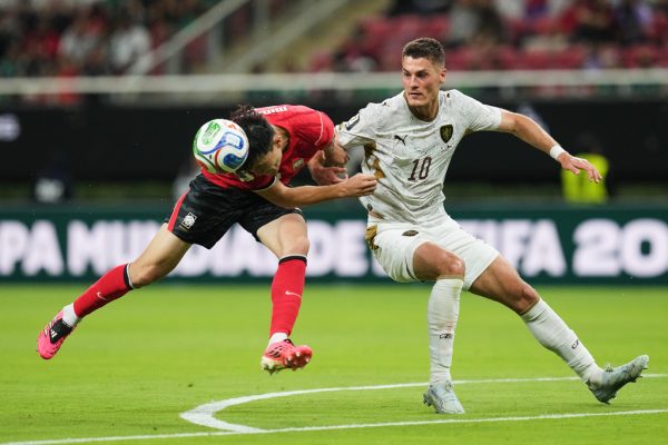 Soccer player heads the ball while another player runs next to him.